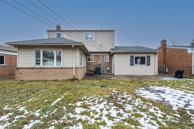 snow covered property with cooling unit, brick siding, fence, a yard, and a chimney