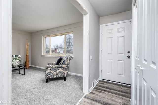 carpeted foyer featuring baseboards and wood finished floors