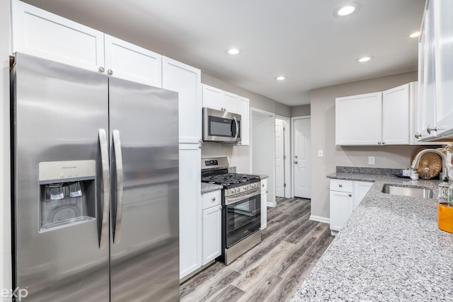 kitchen featuring stainless steel appliances, a sink, white cabinetry, and light stone countertops