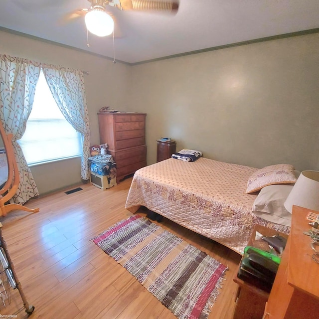 bedroom with a ceiling fan, visible vents, ornamental molding, and wood finished floors