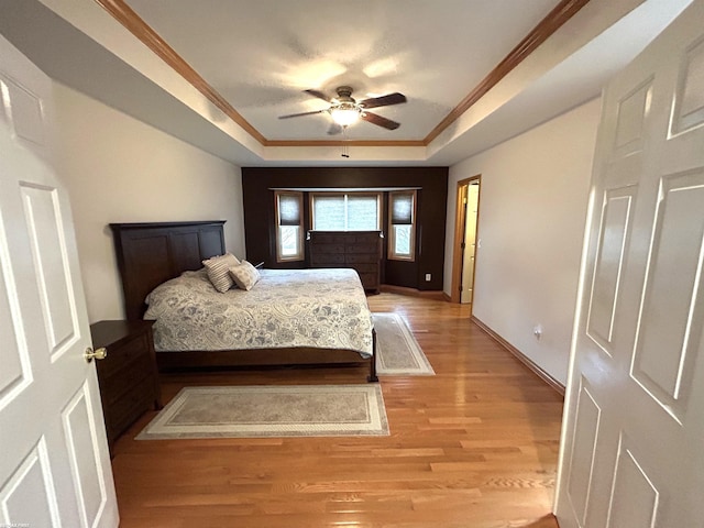 bedroom featuring crown molding, a raised ceiling, light wood-style flooring, ceiling fan, and baseboards