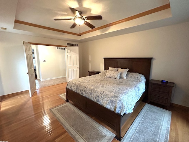 bedroom with light wood-style floors, baseboards, visible vents, and a raised ceiling