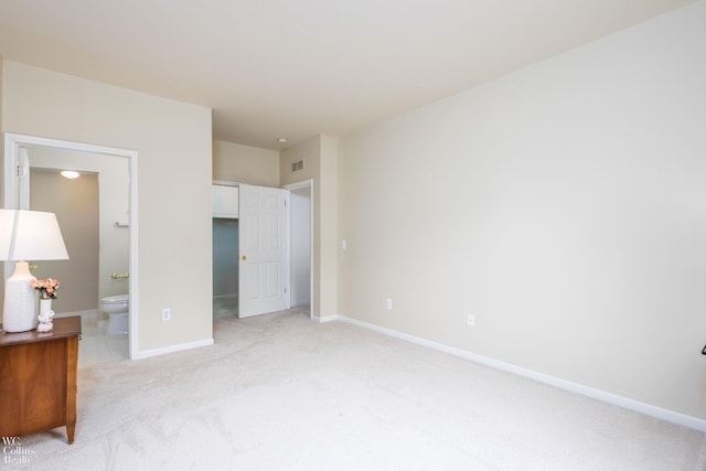 unfurnished bedroom featuring connected bathroom, light carpet, baseboards, a closet, and a walk in closet