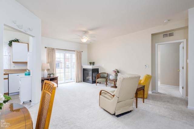 living room with baseboards, visible vents, a ceiling fan, a glass covered fireplace, and light colored carpet