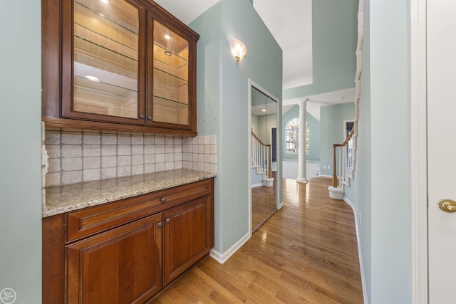 hall featuring baseboards, stairs, light wood-style floors, and decorative columns