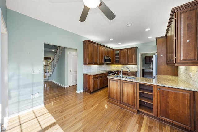 kitchen with a sink, stainless steel microwave, light stone counters, and light wood finished floors