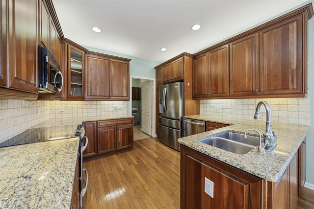 kitchen with glass insert cabinets, light stone countertops, light wood-type flooring, appliances with stainless steel finishes, and a sink