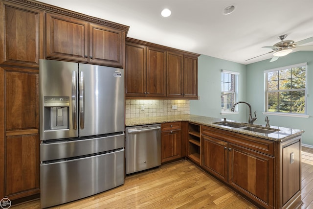 kitchen with a peninsula, light wood-style flooring, a sink, appliances with stainless steel finishes, and tasteful backsplash