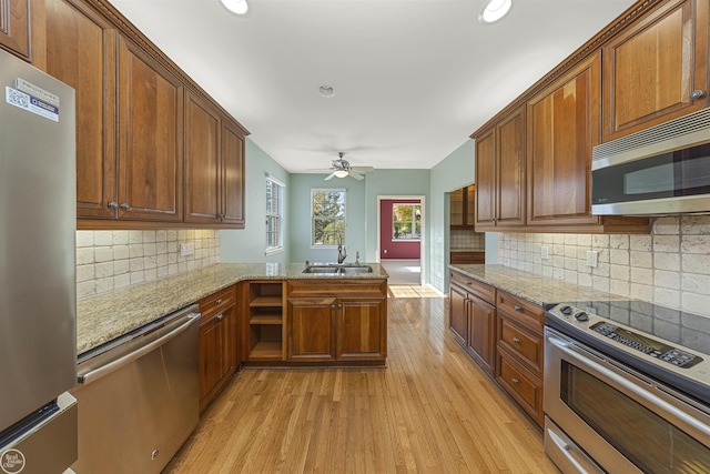 kitchen with a peninsula, light wood-style floors, brown cabinetry, stainless steel appliances, and a sink