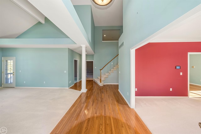 interior space featuring baseboards, high vaulted ceiling, stairs, and ornate columns