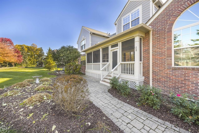 view of exterior entry with a lawn and brick siding