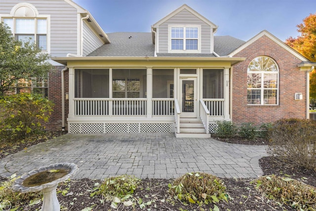 view of front of home with brick siding, a shingled roof, and a sunroom