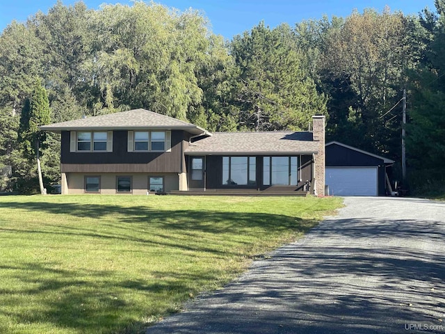 split level home featuring an outbuilding, a shingled roof, a chimney, and a front yard