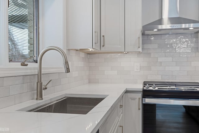 kitchen with gas range, wall chimney exhaust hood, light stone countertops, white cabinetry, and a sink