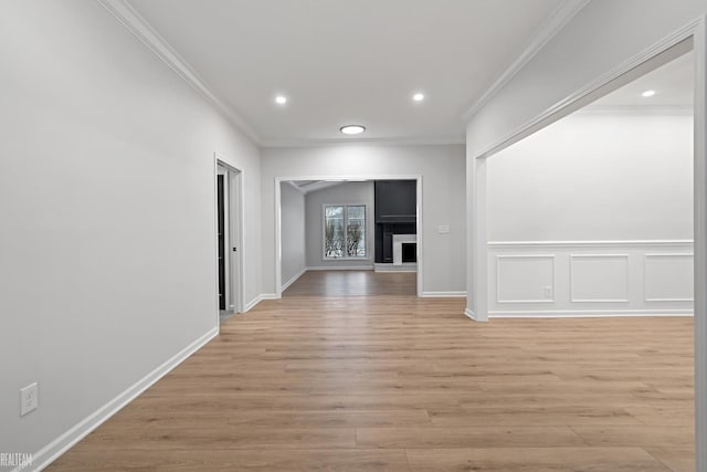 unfurnished room with a fireplace with raised hearth, light wood-style flooring, and crown molding