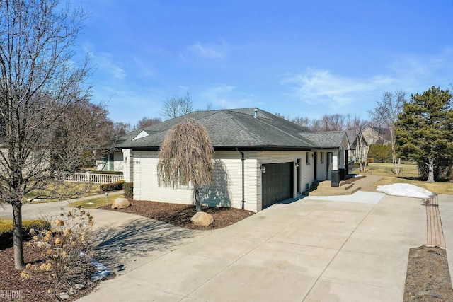 view of property exterior featuring brick siding, a shingled roof, fence, a garage, and driveway