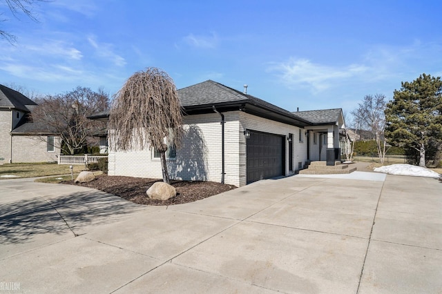 view of side of property featuring brick siding, roof with shingles, concrete driveway, fence, and a garage