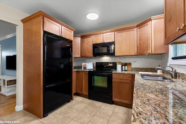 kitchen featuring black appliances, dark stone countertops, light tile patterned floors, and a sink