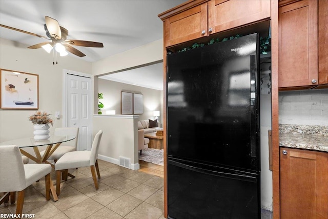 kitchen with brown cabinetry, freestanding refrigerator, light tile patterned flooring, and backsplash