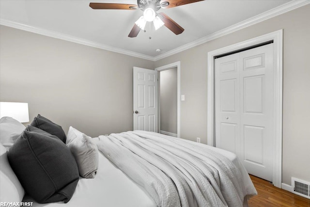 bedroom featuring crown molding, a closet, visible vents, a ceiling fan, and wood finished floors