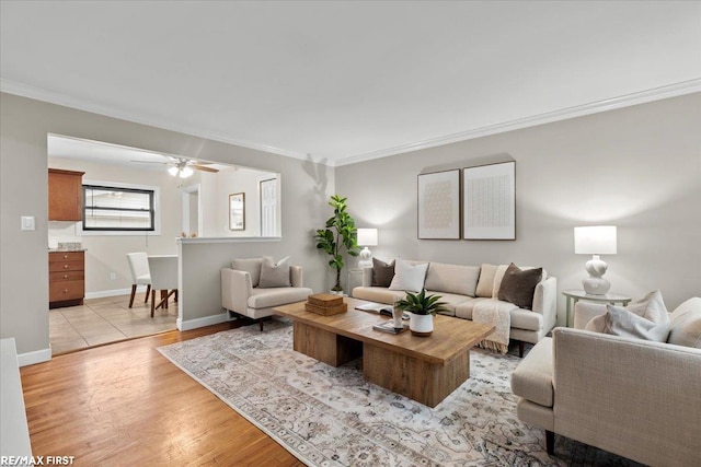 living room with light wood finished floors, ornamental molding, a ceiling fan, and baseboards