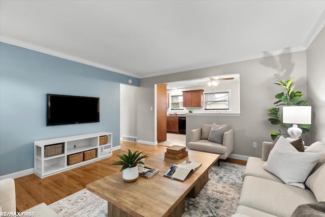 living room with light wood-type flooring, visible vents, crown molding, and baseboards