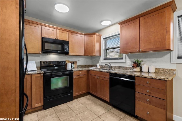 kitchen with light stone counters, brown cabinets, black appliances, a sink, and light tile patterned flooring