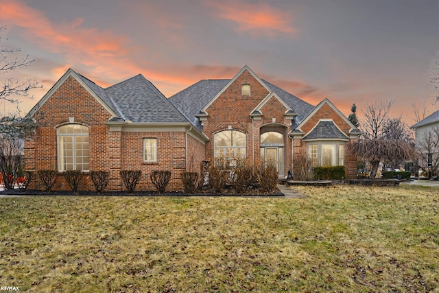 view of front of house featuring a shingled roof, brick siding, and a yard