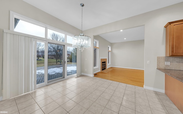 unfurnished dining area with a fireplace, recessed lighting, light tile patterned flooring, a chandelier, and baseboards