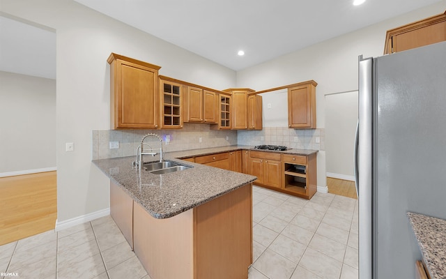 kitchen featuring a peninsula, a sink, freestanding refrigerator, and decorative backsplash