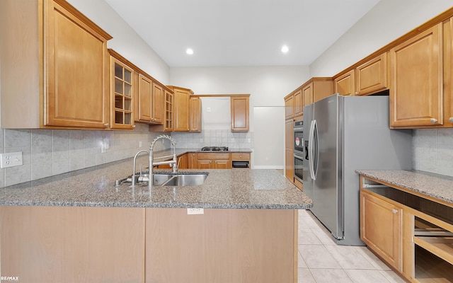 kitchen featuring tasteful backsplash, glass insert cabinets, a peninsula, stainless steel appliances, and a sink