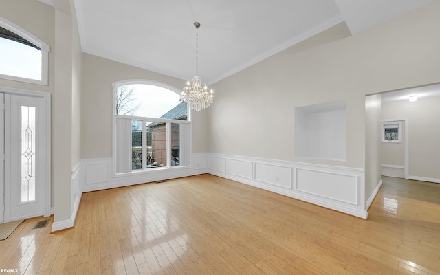 entryway with a chandelier, wainscoting, light wood-type flooring, high vaulted ceiling, and a decorative wall