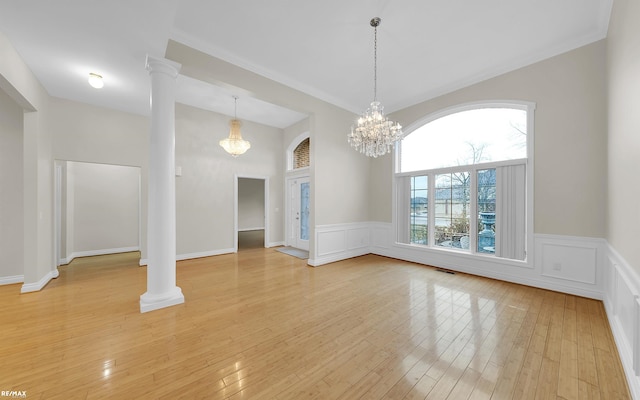 unfurnished dining area with decorative columns, a decorative wall, light wood finished floors, and an inviting chandelier