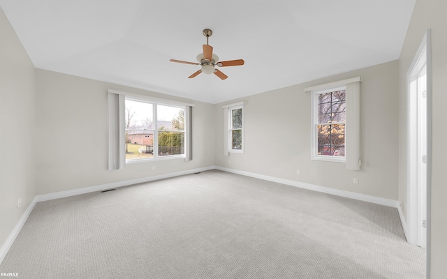 carpeted spare room with a ceiling fan, a wealth of natural light, visible vents, and baseboards