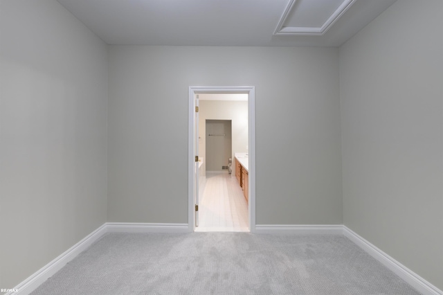 spare room featuring attic access, baseboards, and light colored carpet