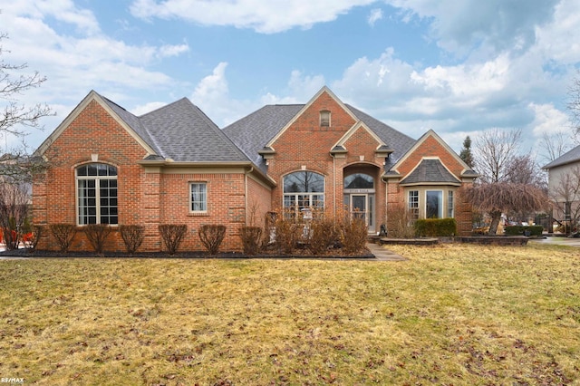 view of front of property featuring brick siding, a front lawn, and roof with shingles