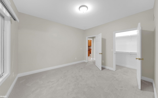 unfurnished bedroom featuring a walk in closet, a closet, light carpet, and baseboards