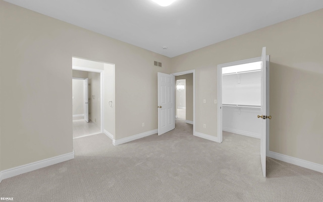 unfurnished bedroom featuring baseboards, visible vents, light colored carpet, a walk in closet, and a closet