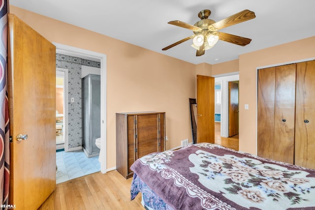 bedroom featuring baseboards, ensuite bath, ceiling fan, light wood-type flooring, and a closet