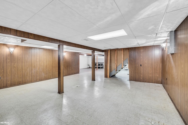 finished below grade area with wooden walls, a drop ceiling, and tile patterned floors