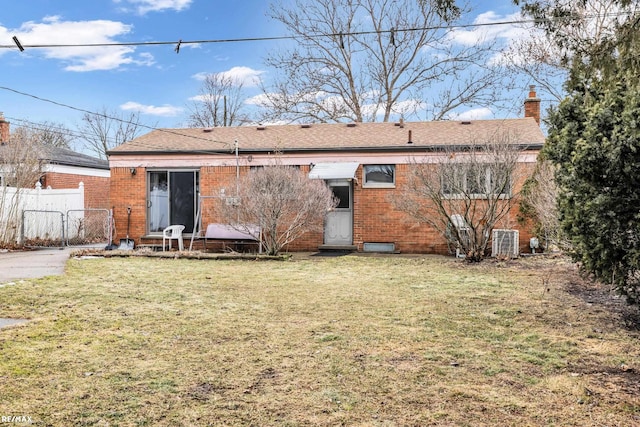 back of house featuring brick siding, a lawn, a chimney, and fence