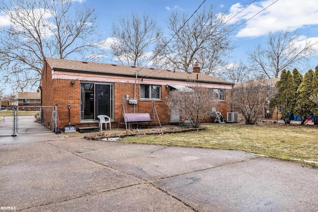 view of front of property featuring brick siding, a chimney, central AC unit, a gate, and a front lawn