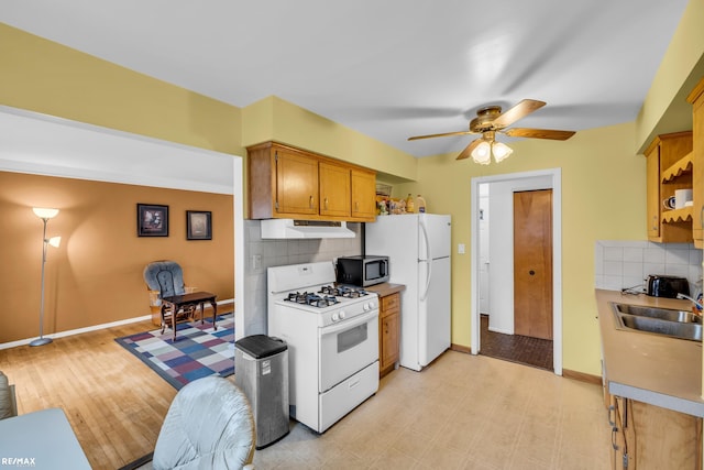 kitchen with brown cabinets, decorative backsplash, a sink, white appliances, and exhaust hood