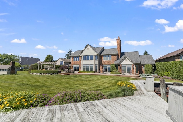 back of property with brick siding, a chimney, a lawn, a deck, and a pergola