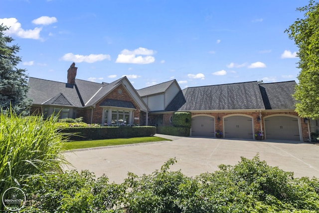 view of front of home featuring an attached garage, driveway, a chimney, and brick siding