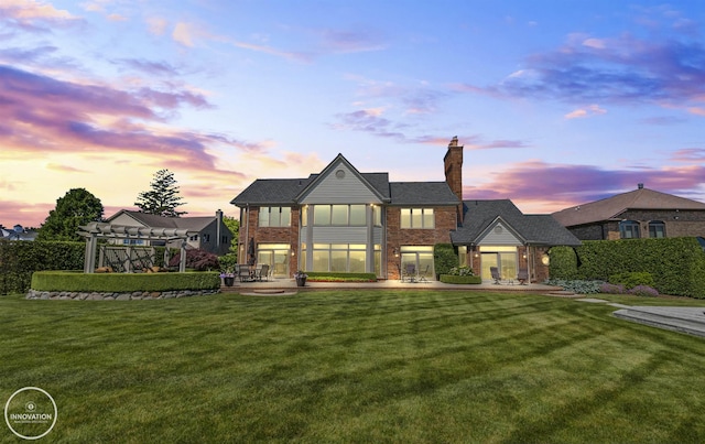 rear view of property featuring a chimney, a yard, a patio area, a pergola, and brick siding