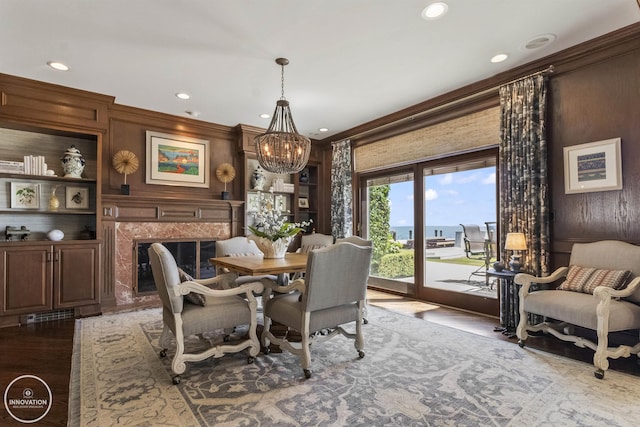 dining space featuring built in features, wood finished floors, crown molding, a notable chandelier, and a high end fireplace