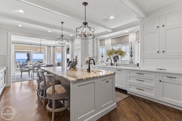 kitchen with dark wood finished floors, an island with sink, a kitchen breakfast bar, white cabinetry, and beam ceiling