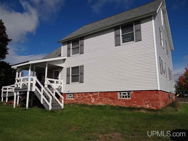 rear view of property with stairway and a lawn