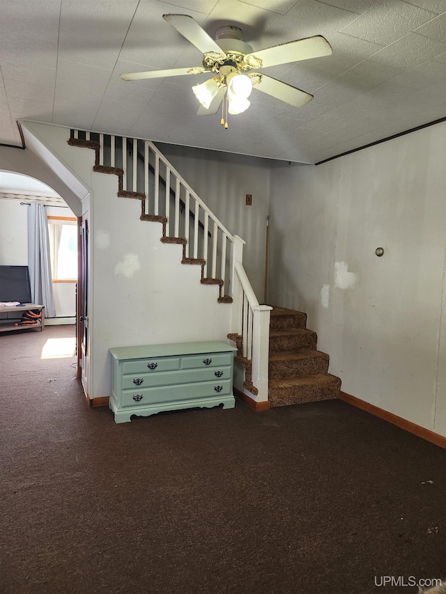 basement featuring a ceiling fan, dark colored carpet, stairway, and baseboards